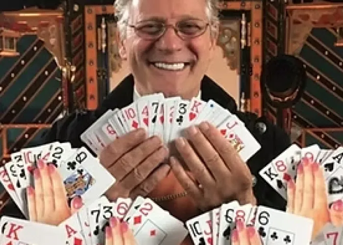 Photo of Lawrence Larouche holding splayed cards, several hands in front of him also holding cards, metal and gears in background